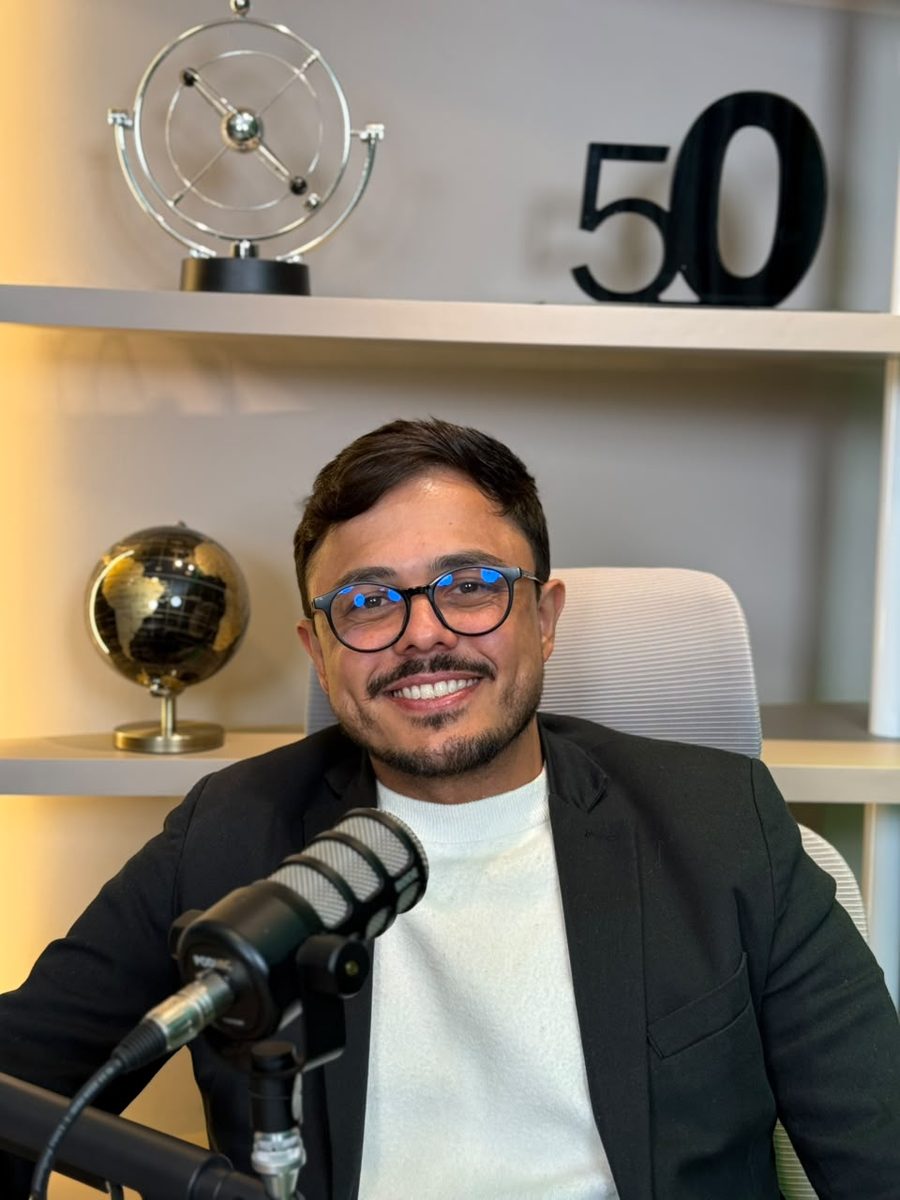 O convidado do episódio 03 no microfone, com o globo e o número 50 na estante atrás.