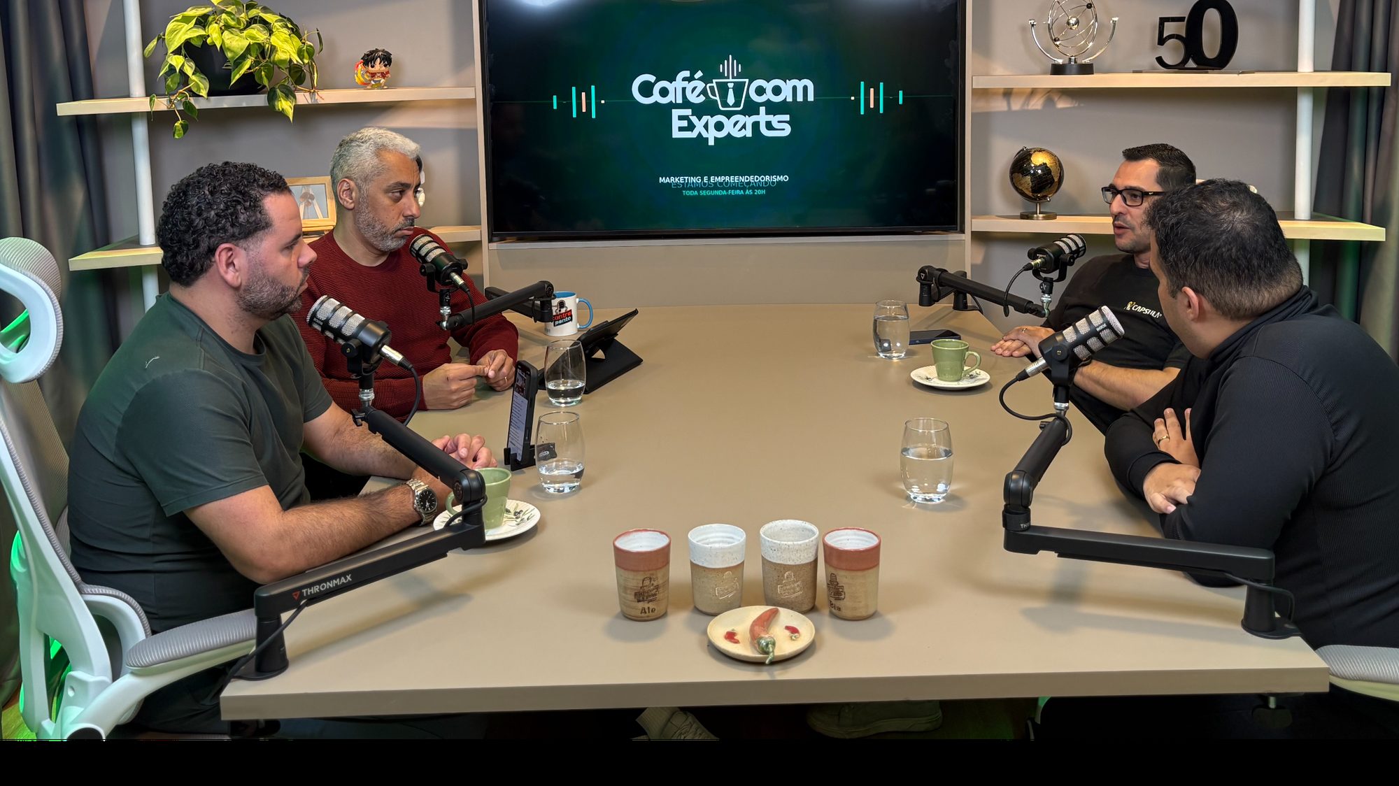 A mesa do programa em uso, no estúdio do ContraPonto, com os microfones e as xícaras.